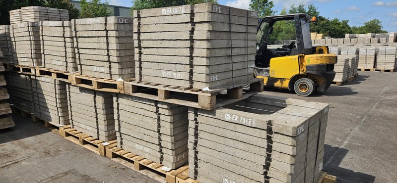 Forklift moving pallets of precast concrete units across a storage yard