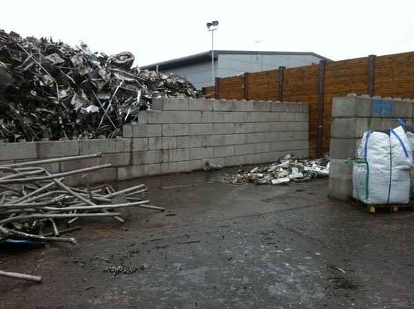 Duo block wall retaining piled scrap metal in a salvage yard