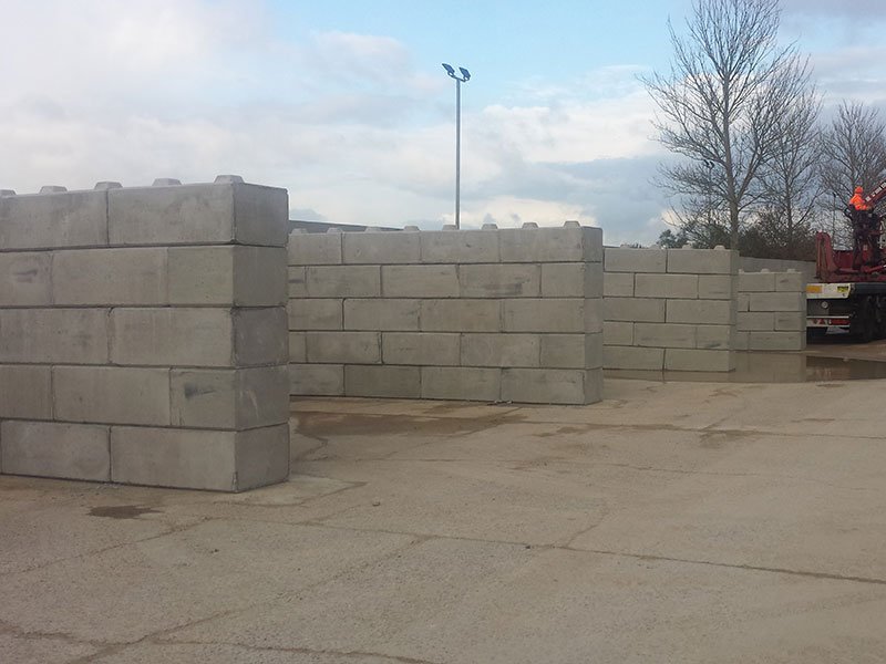 Interlocking block walls forming open storage bays across a concrete yard