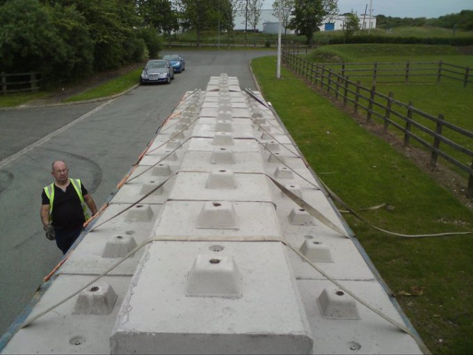 Row of strapped concrete blocks laid along a tarmac lane after delivery