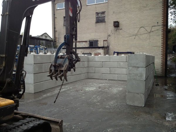 Excavator grab placing Duo blocks to form a storage bay against a building
