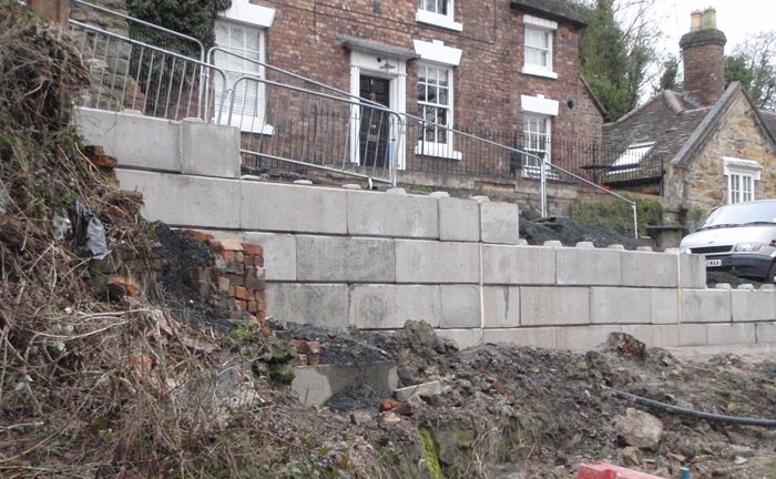 Duo block retaining wall stepped along a cleared slope below stone houses