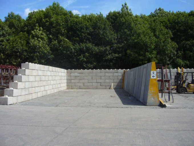 Duo block wall enclosing a yard with a forklift and woodland behind
