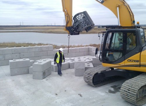 Excavator lifting Duo walling blocks into place while an operative directs