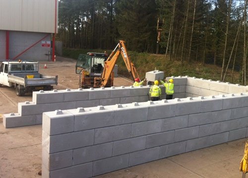 Excavator and workers building a three-sided Duo block bunker on hardstanding