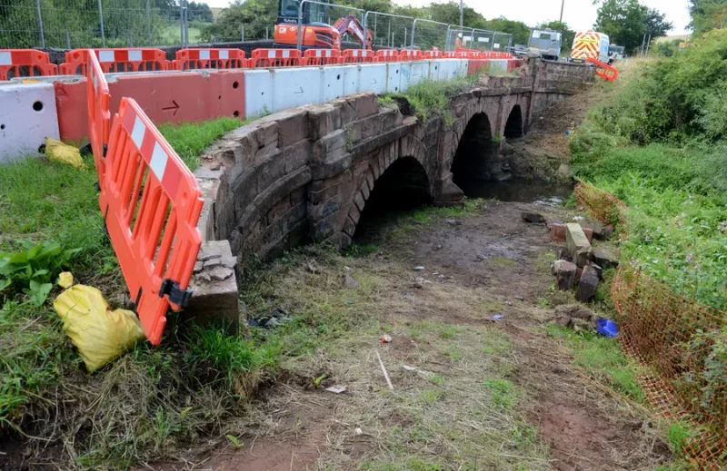 Barriers and fencing along a stone arch bridge above a dry stream bed