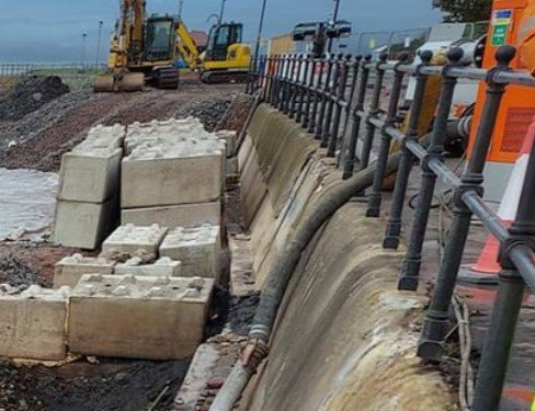 Interlocking blocks placed along a coastal sea wall beside iron railings