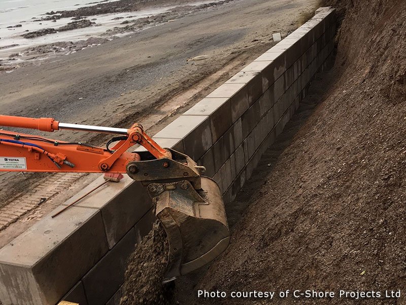 Excavator working on the beach beside a Legato block sea wall