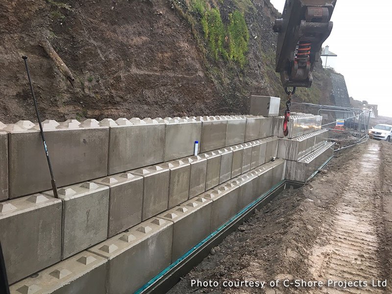 Crane lowering a Legato block onto a long coastal defence wall