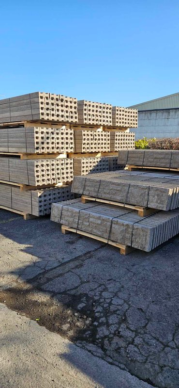 Pallets of concrete fence posts and gravel boards stacked in a yard