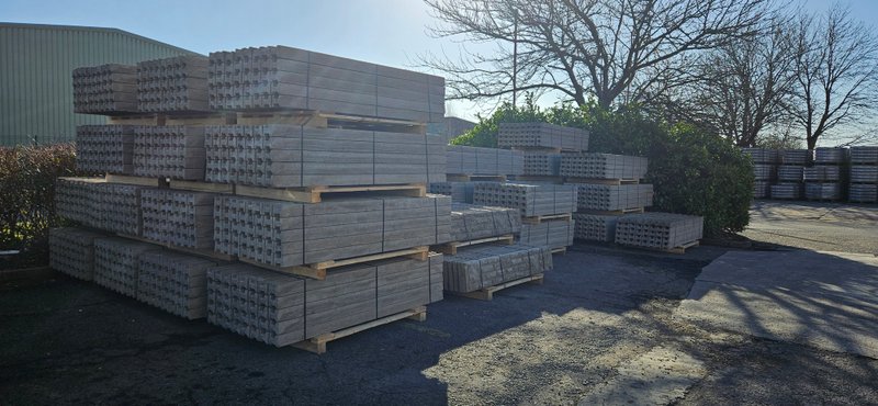Stacks of precast concrete fence posts and gravel boards in a storage yard