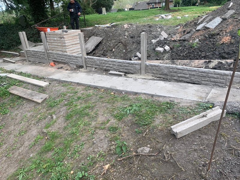 Concrete gravel boards slotted between posts to retain soil in a garden