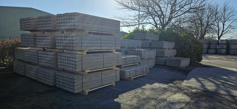 Stacks of precast concrete fence posts and gravel boards in a storage yard