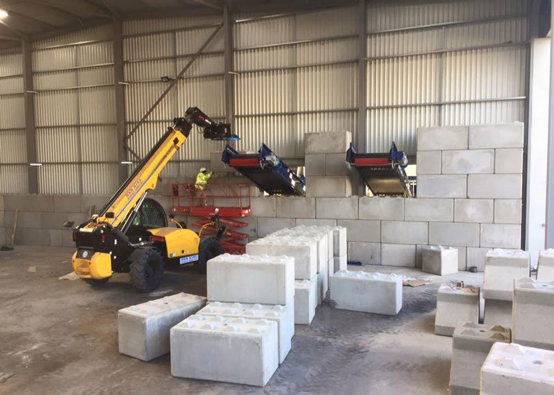 Telehandler lifting Legato interlocking blocks to build a wall under a recycling conveyor