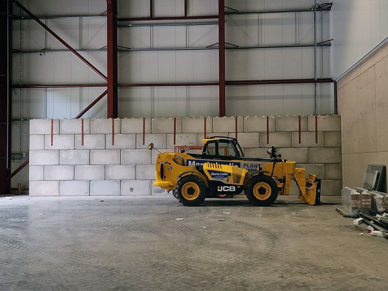 Interlocking block wall inside a warehouse with a telehandler parked alongside