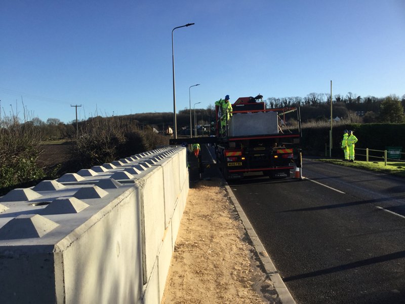 Interlocking block flood protection wall being installed along a rural roadside