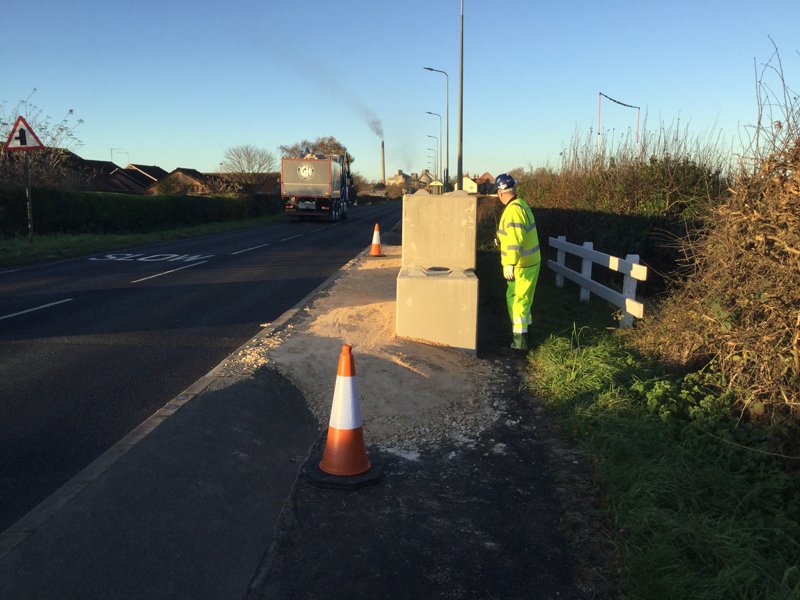 Two interlocking blocks placed on a roadside verge beside a traffic cone