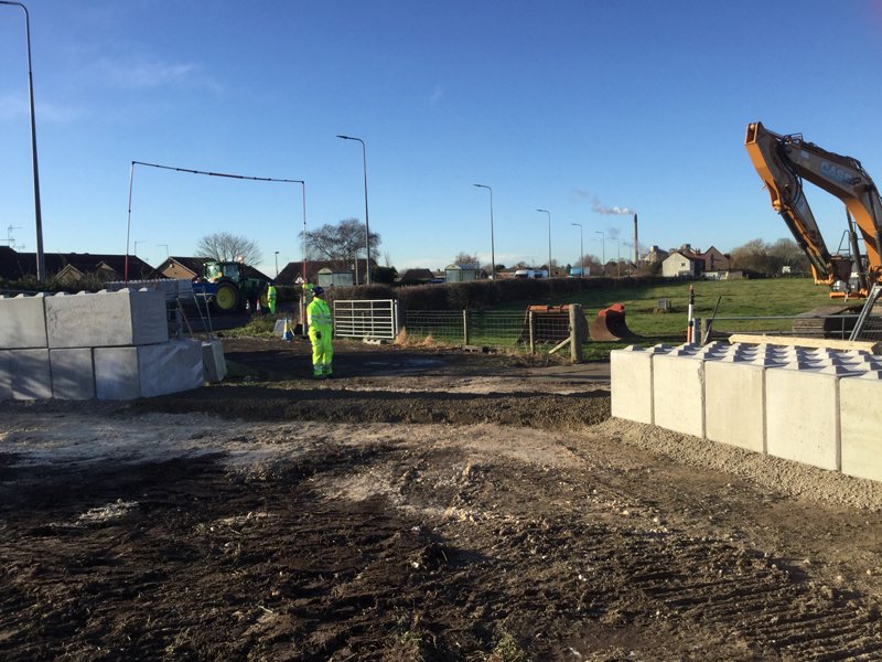 Interlocking blocks being positioned by excavator to form a flood defence wall