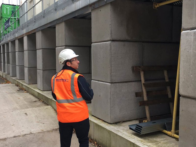 Worker in hi-vis standing beside a stacked interlocking block wall on flood works