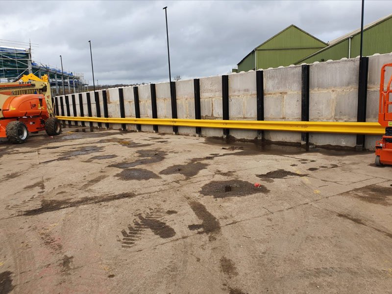 Precast flood wall panels between steel posts running across a wet yard