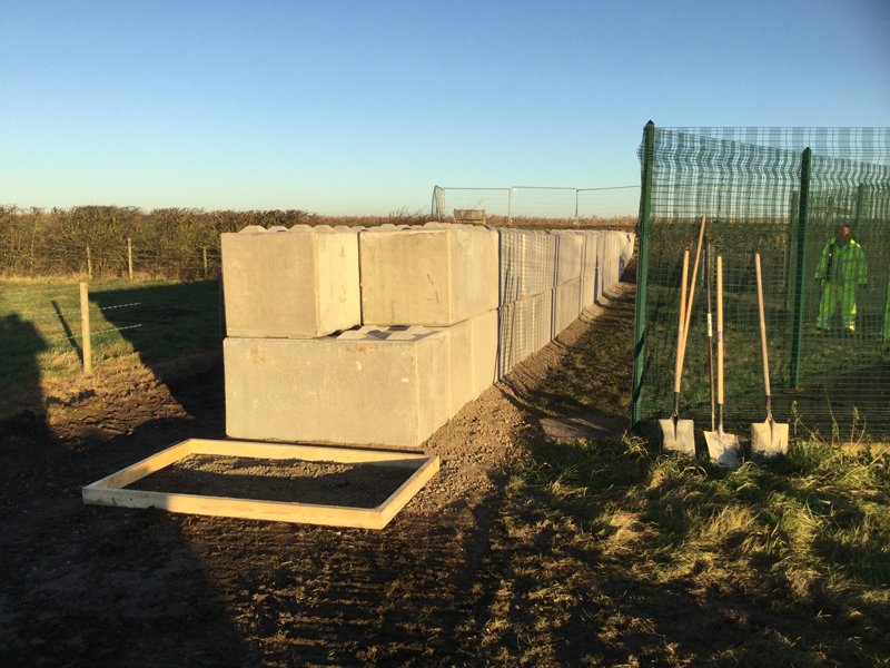 Large interlocking blocks stacked beside green site fencing with shovels ready