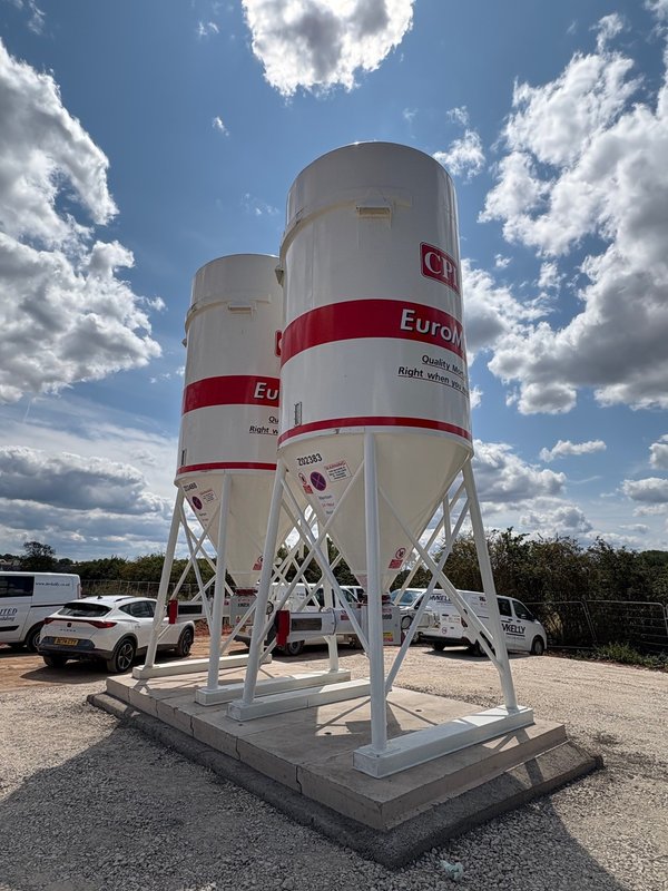 Pair of cement silos on precast silo foundation base slabs beside parked vehicles