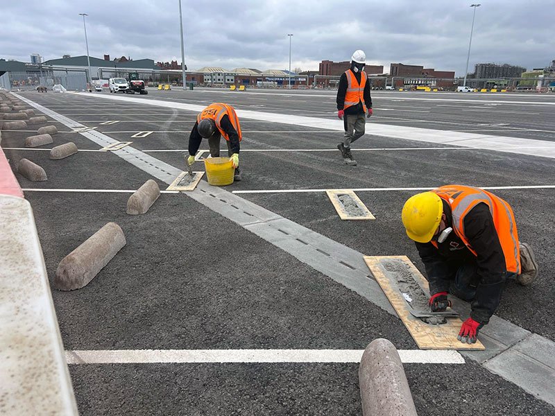 Workers in hi-vis installing precast HGV wheel stops on marked parking bays