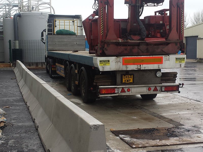 Jersey barriers protecting a wet industrial yard beside a flatbed crane lorry