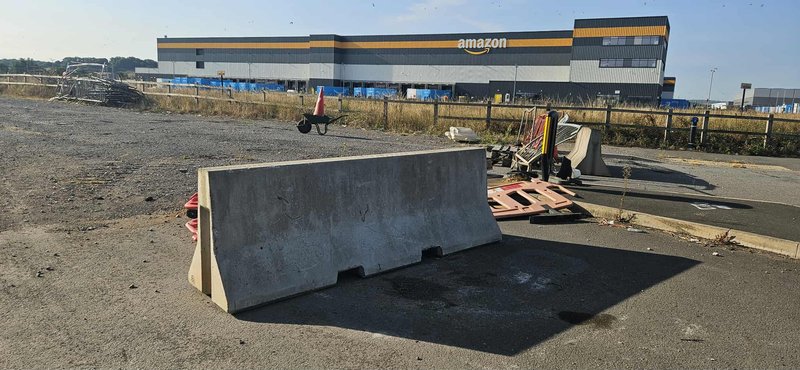 Concrete security barrier on open ground in front of a distribution warehouse