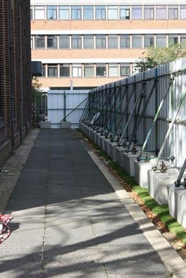 Duo blocks anchoring a braced site hoarding beside an office footpath