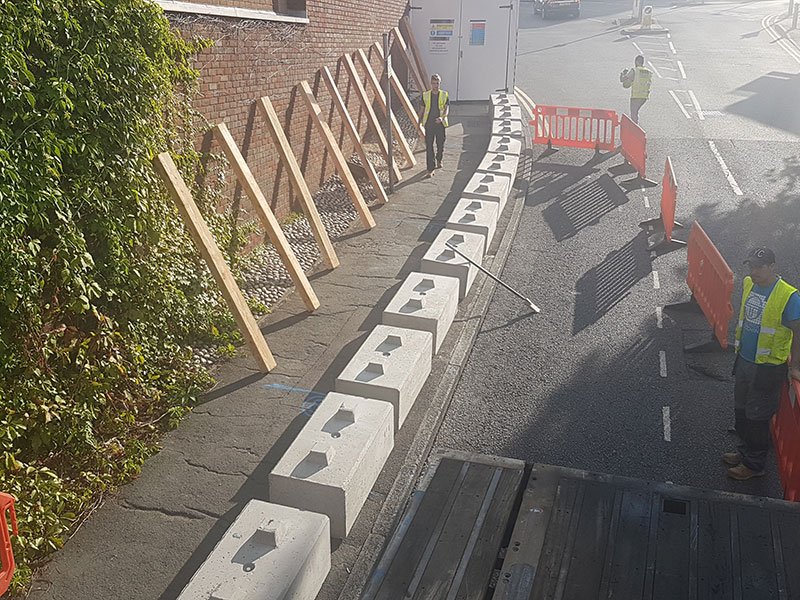Timber-propped hoarding blocks installed along a roadside with workers in high-vis