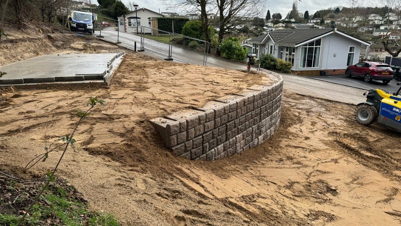 Curved cobblestone-finish retaining wall built on a sandy holiday park plot