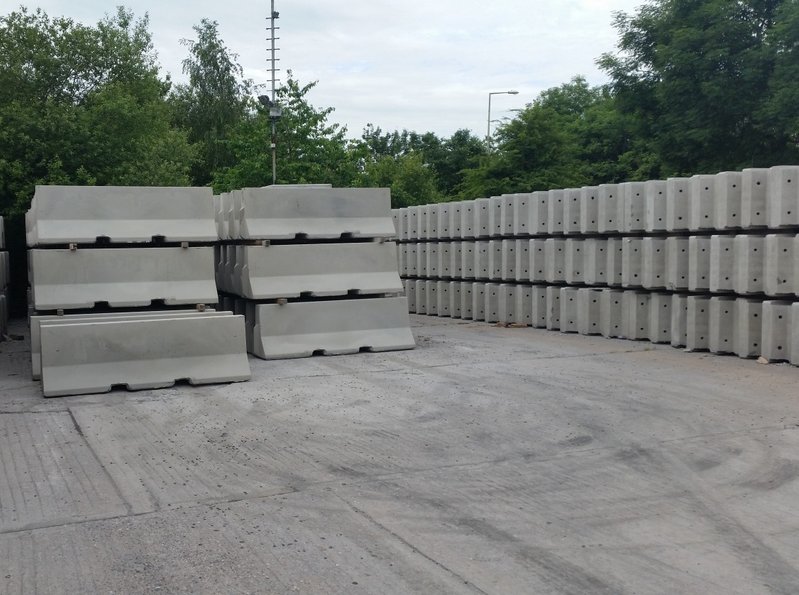 Stacked Jersey barriers beside long rows of units in a storage yard