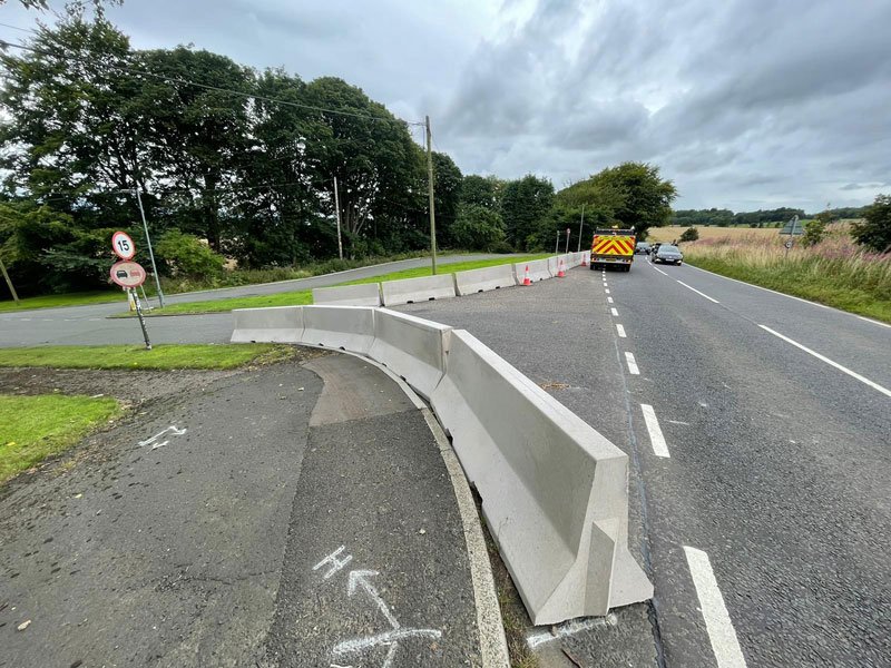 Curved run of Jersey barriers separating a verge from a rural carriageway