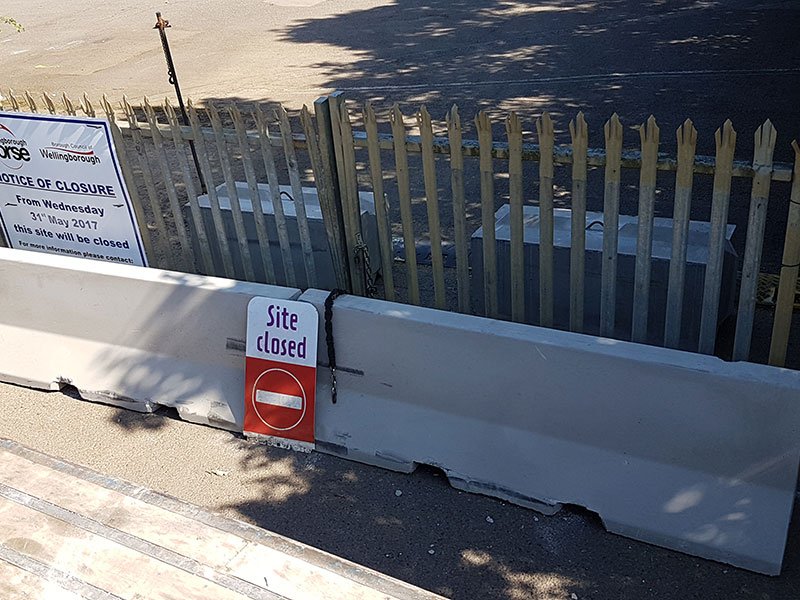 Jersey barrier closing a palisade gateway with a site closed sign attached