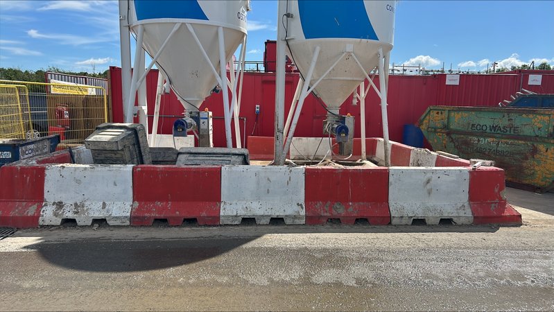 Site silos on precast foundation slabs behind a run of red and white barriers