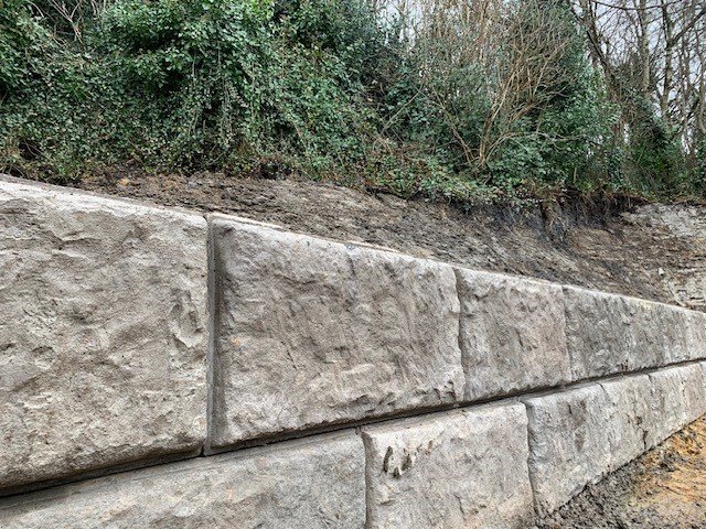 Rock-faced Vee-Rock retaining wall built against a steep vegetated hillside bank