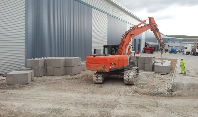 Excavator placing Legato blocks to form a retaining wall beside a warehouse