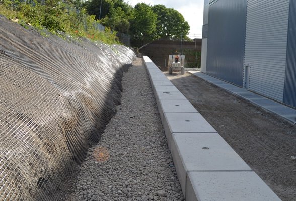 Line of flat-topped Legato blocks edging a track beside a mesh-faced embankment