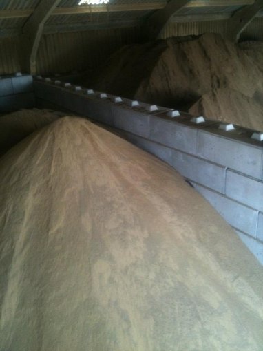 Sand stockpile filling a block-walled storage bay under a timber roof