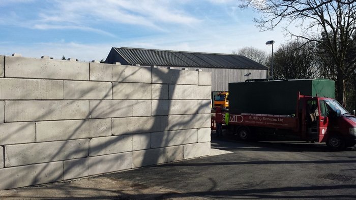 Duo block wall enclosing a commercial yard with lorries parked behind