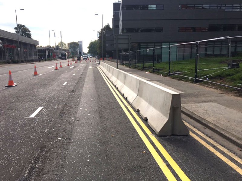 Continuous run of Jersey barriers dividing a roadway beside fenced ground