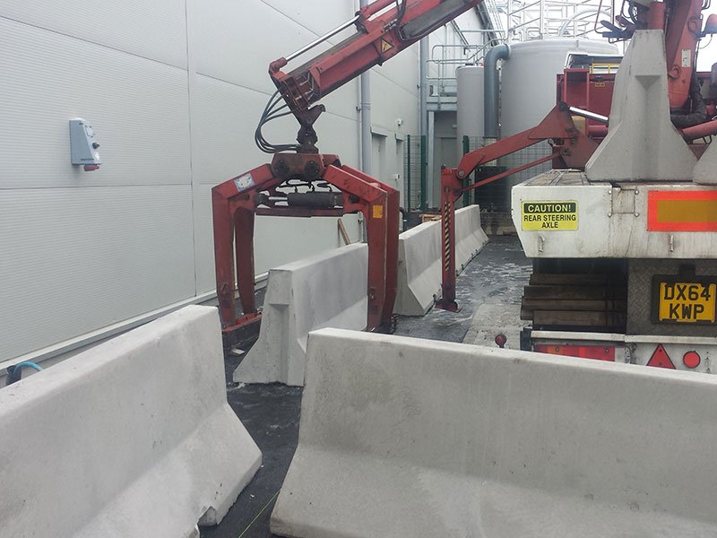 Lorry-mounted grab lifting a Jersey barrier into position against a wall