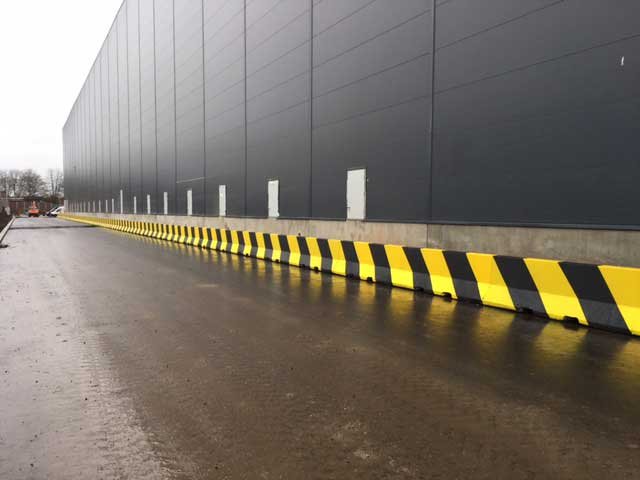 Jersey barriers painted with black and yellow hazard stripes along a warehouse wall