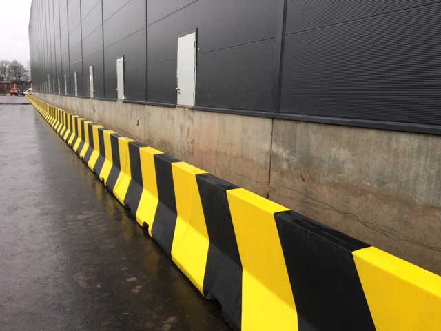 Run of Jersey barriers painted with yellow and black chevrons along a building
