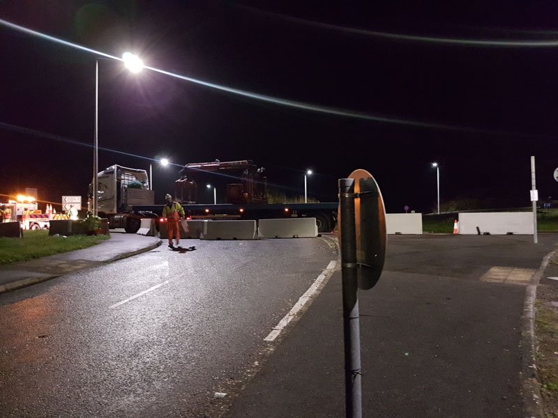 Night road closure with a worker placing Jersey barriers across the carriageway