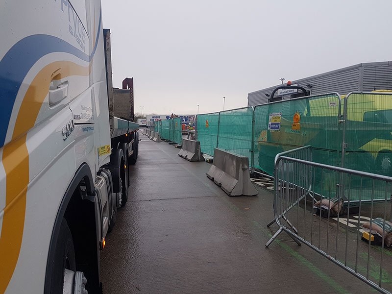 Jersey barriers being installed along a site perimeter beside green mesh fencing