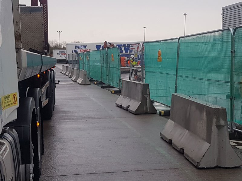 Jersey barriers set out along fencing while a delivery lorry waits on the road