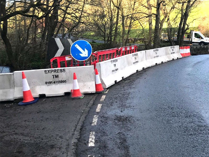 Curved run of barriers with cones and a keep-left sign on a wet road