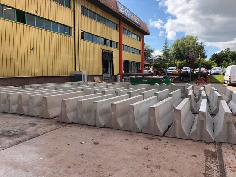 Rows of Jersey barriers stored in a yard outside a factory building